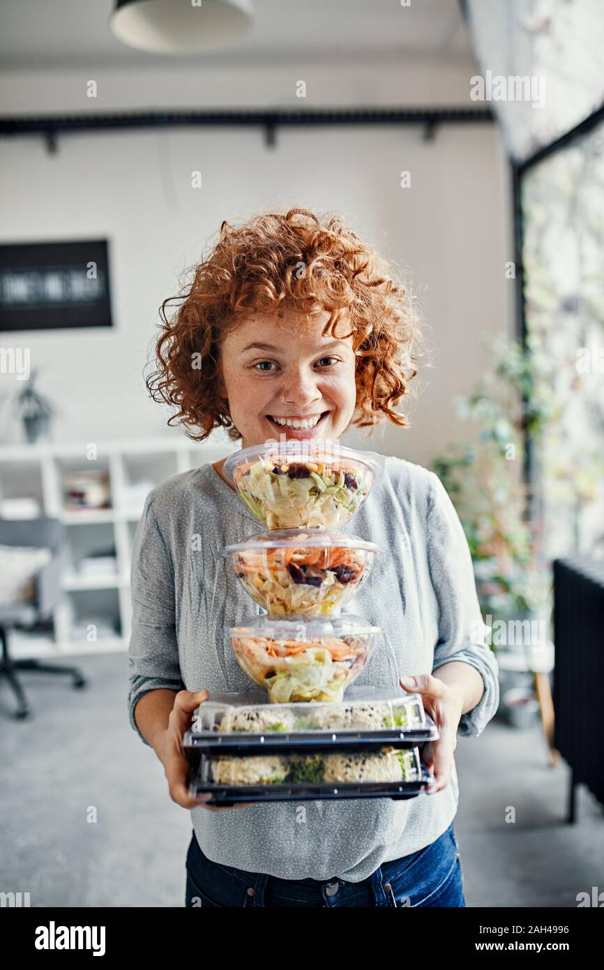Ritratto di sorridere imprenditrice stack di contenimento di cibo da asporto in office Foto Stock