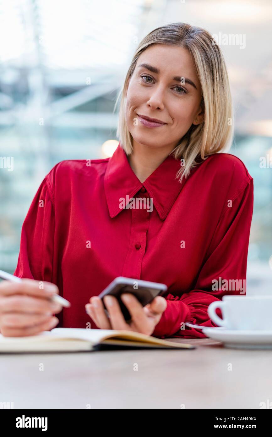 Ritratto di giovane imprenditrice con un telefono cellulare a prendere appunti in un cafe Foto Stock