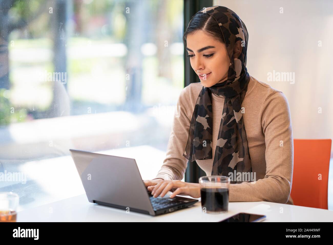 Giovane donna indossa velo utilizzando laptop in un cafe Foto Stock