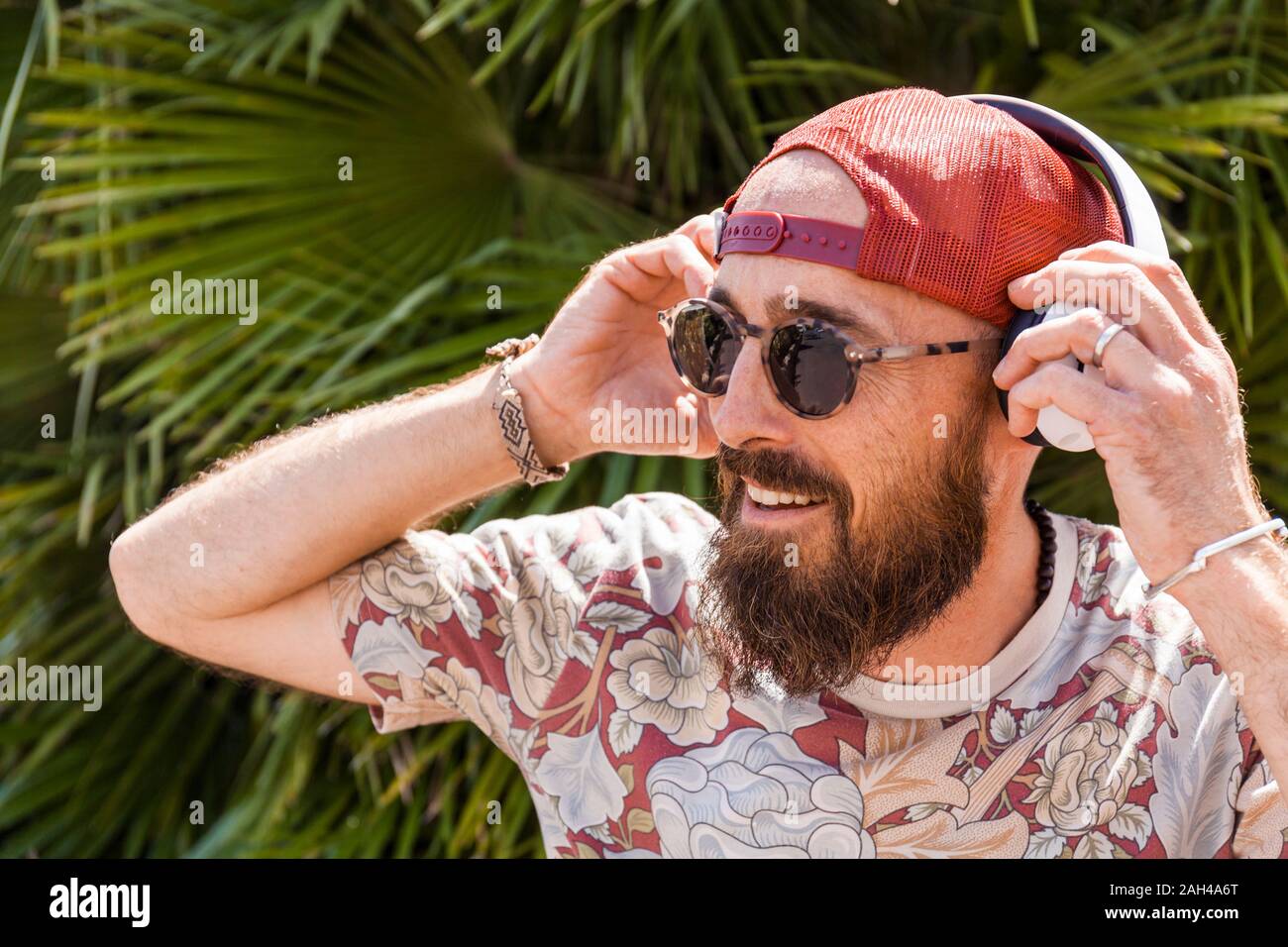 Sorridente uomo maturo con red basecap, occhiali da sole e cuffie bianche Foto Stock