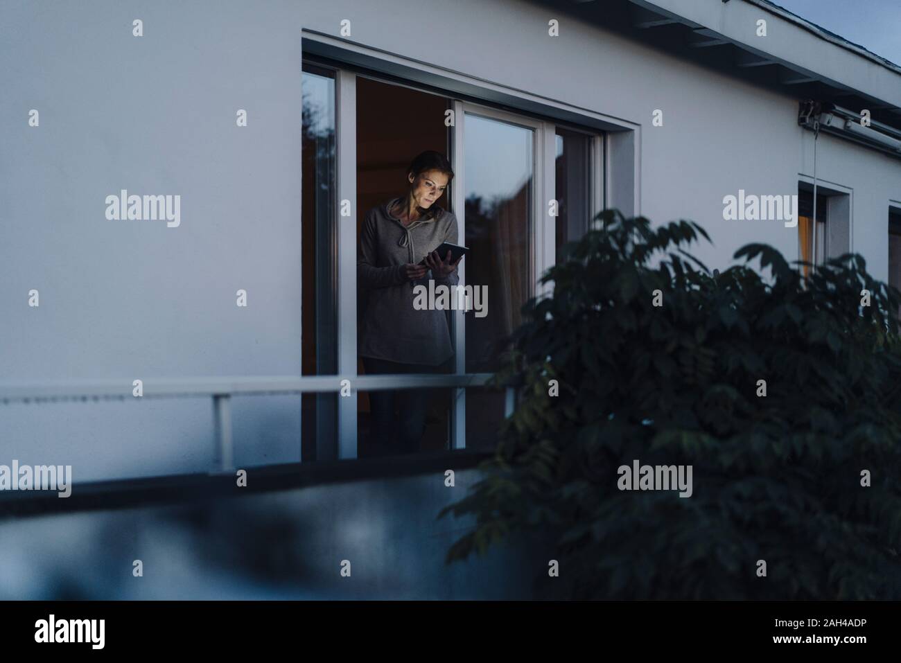 Donna in piedi nella porta del balcone, utilizzando tavoletta digitale Foto Stock