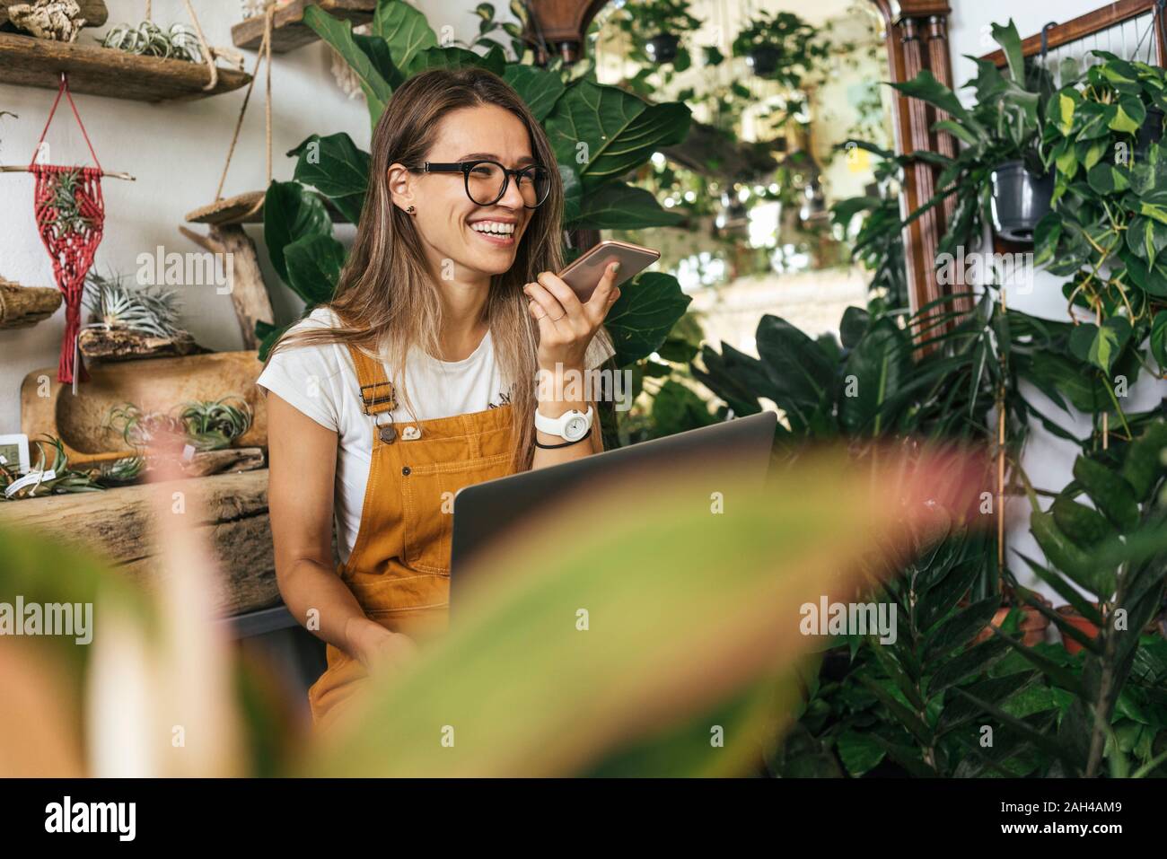 Felice giovane donna utilizza lo smartphone in un piccolo negozio di giardinaggio Foto Stock