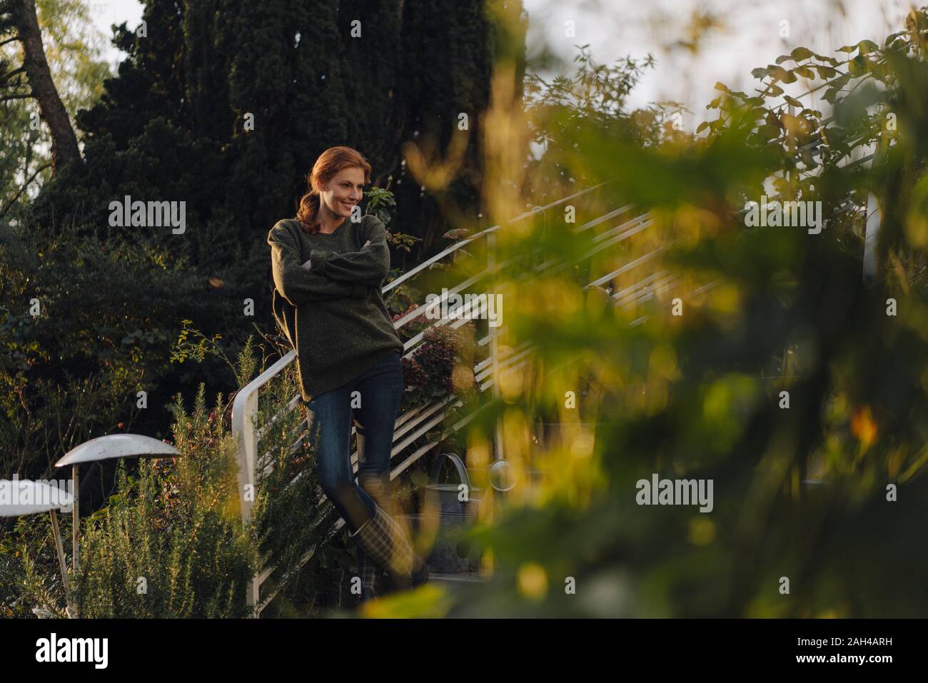 Felice donna in piedi sulle scale nel suo giardino, sorridente Foto Stock