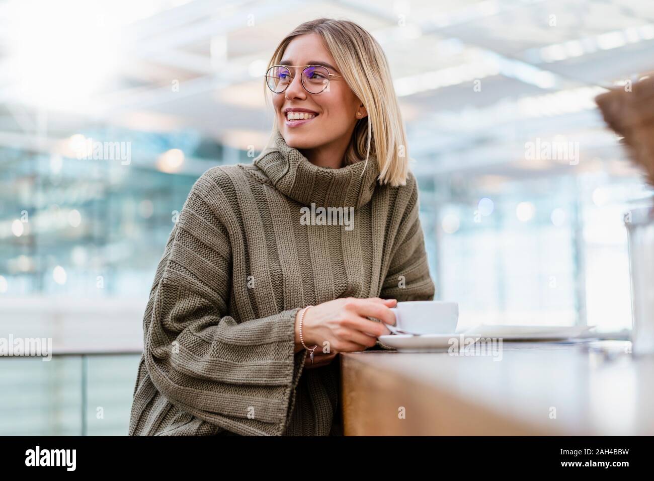 Ritratto di un sorridente giovane donna in una caffetteria che guarda lontano Foto Stock