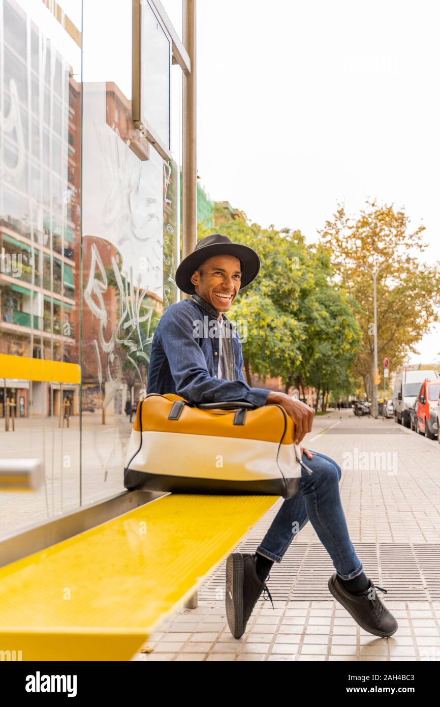 Ridendo elegante giovane uomo in attesa presso la fermata degli autobus nella città Foto Stock