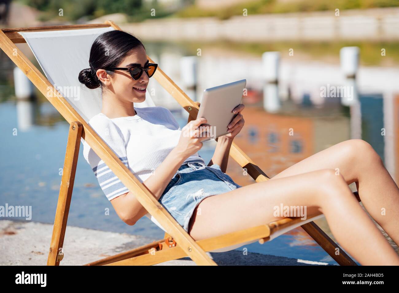 Sorridente giovane donna seduto in una sedia a sdraio utilizzando tablet Foto Stock