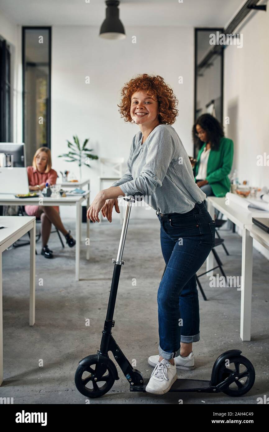 Ritratto di un sorridente imprenditrice con kick scooter in office Foto Stock