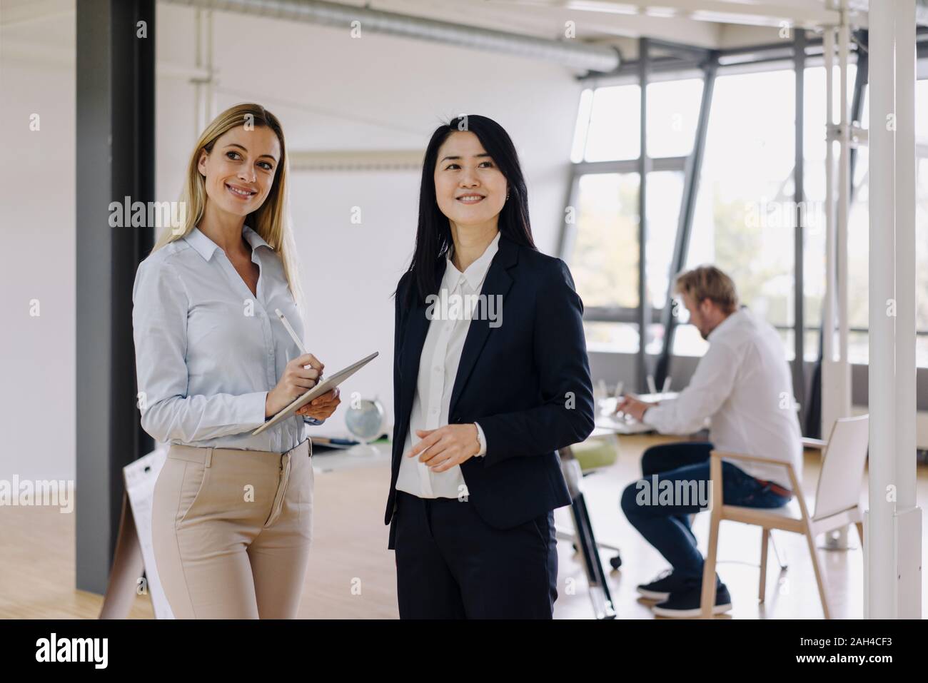 Due imprenditrici con la compressa in office e imprenditore in background Foto Stock