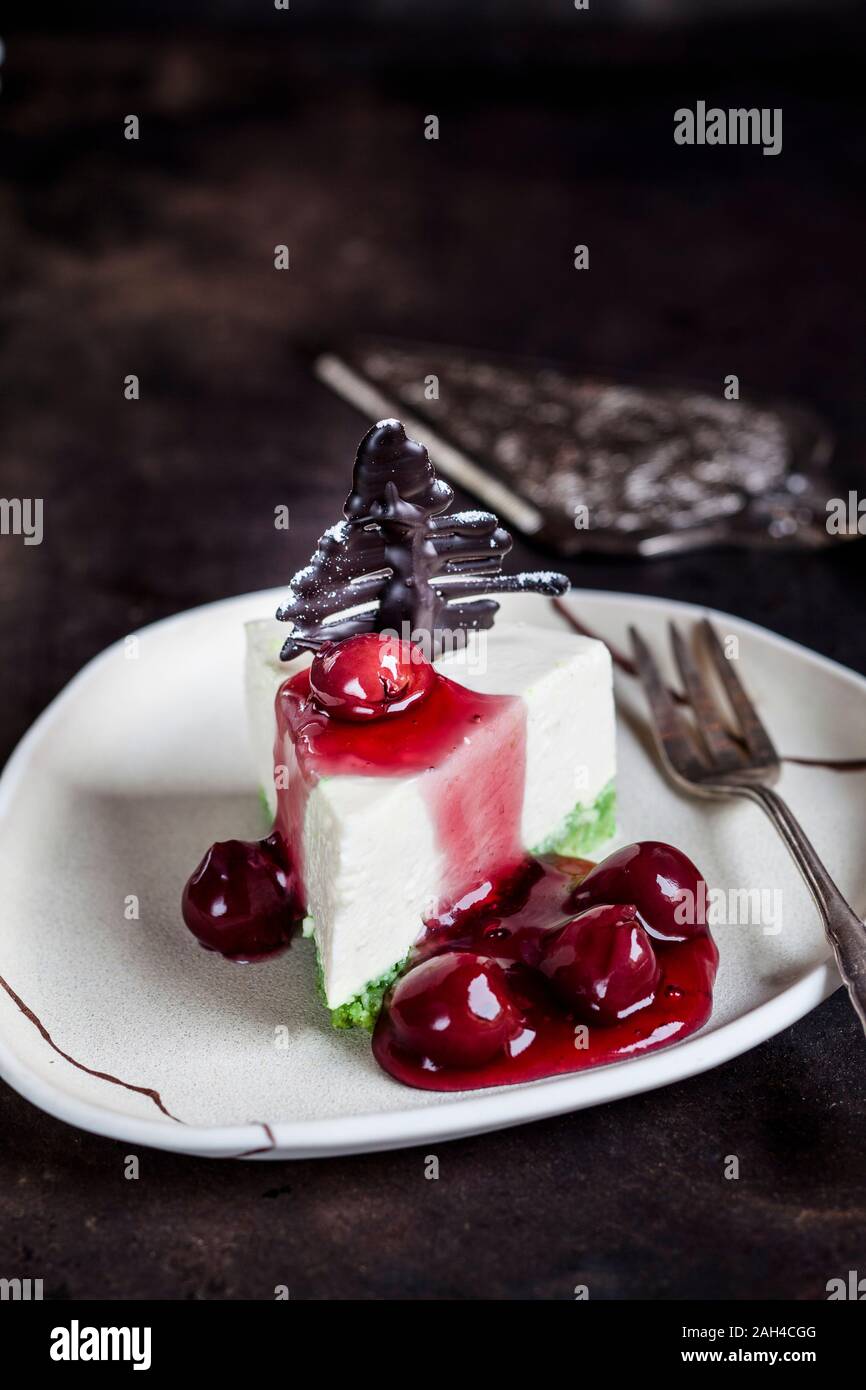 Pezzo di no-bake cheesecake, decorata con cioccolato alberi di Natale sulla piastra calda con salsa alle ciliegie Foto Stock