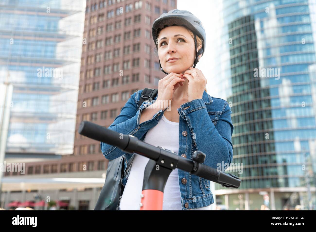 Donna con e-scooter nella città di mettere sul casco, Berlino, Germania Foto Stock