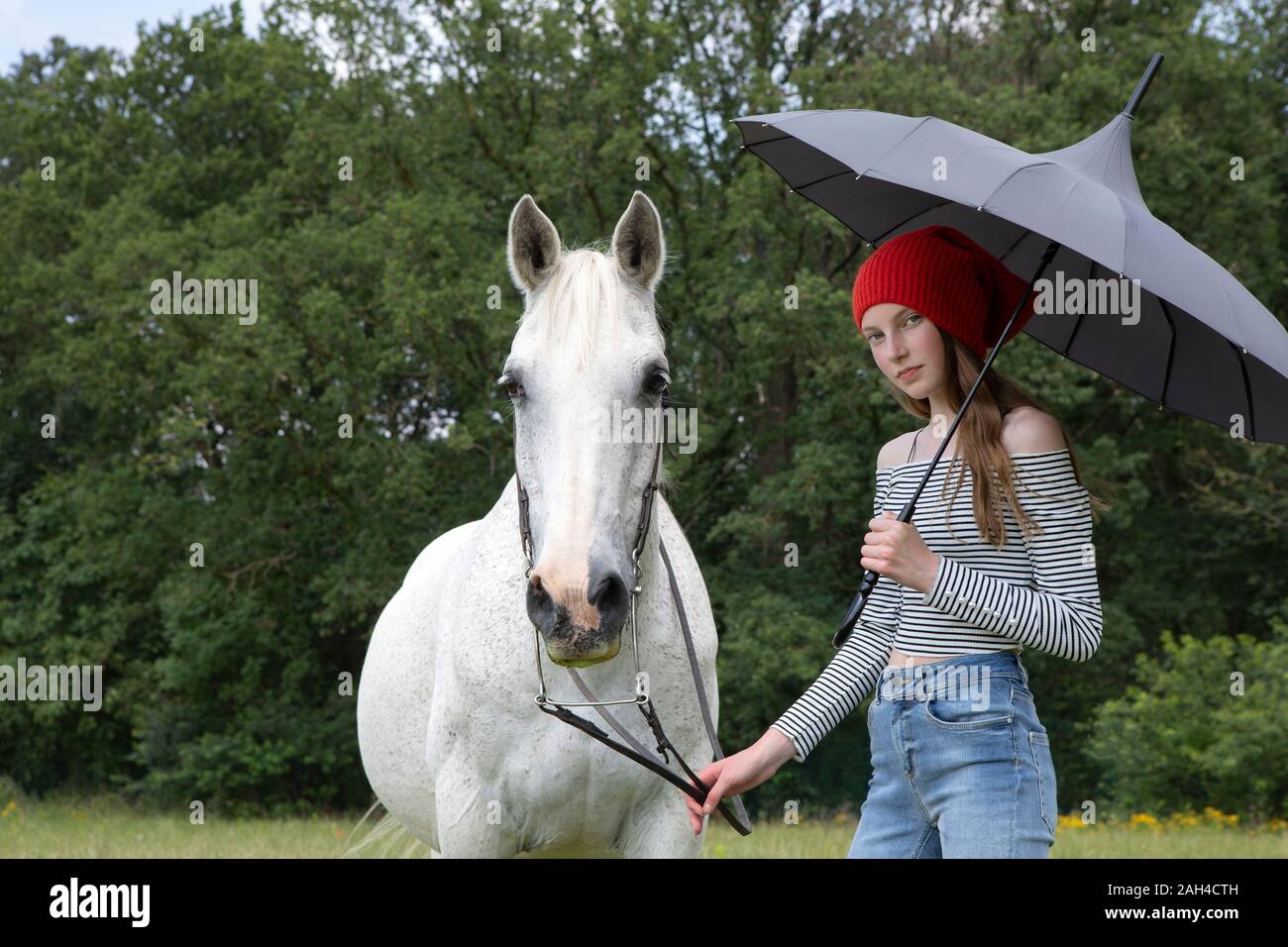 Ritratto di ragazza adolescente in piedi su un prato con cavallo e ombrellone Foto Stock