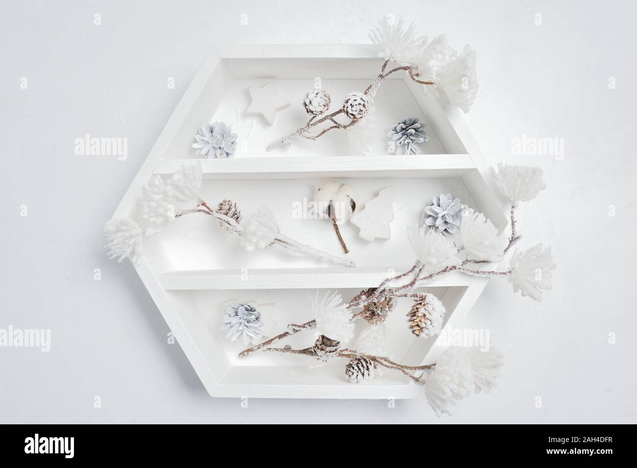 Decorativo libreria bianco con decorazioni di Natale. Coni, fiori di cotone bianco e fiori invernali sul tavolo con posto per il testo Foto Stock