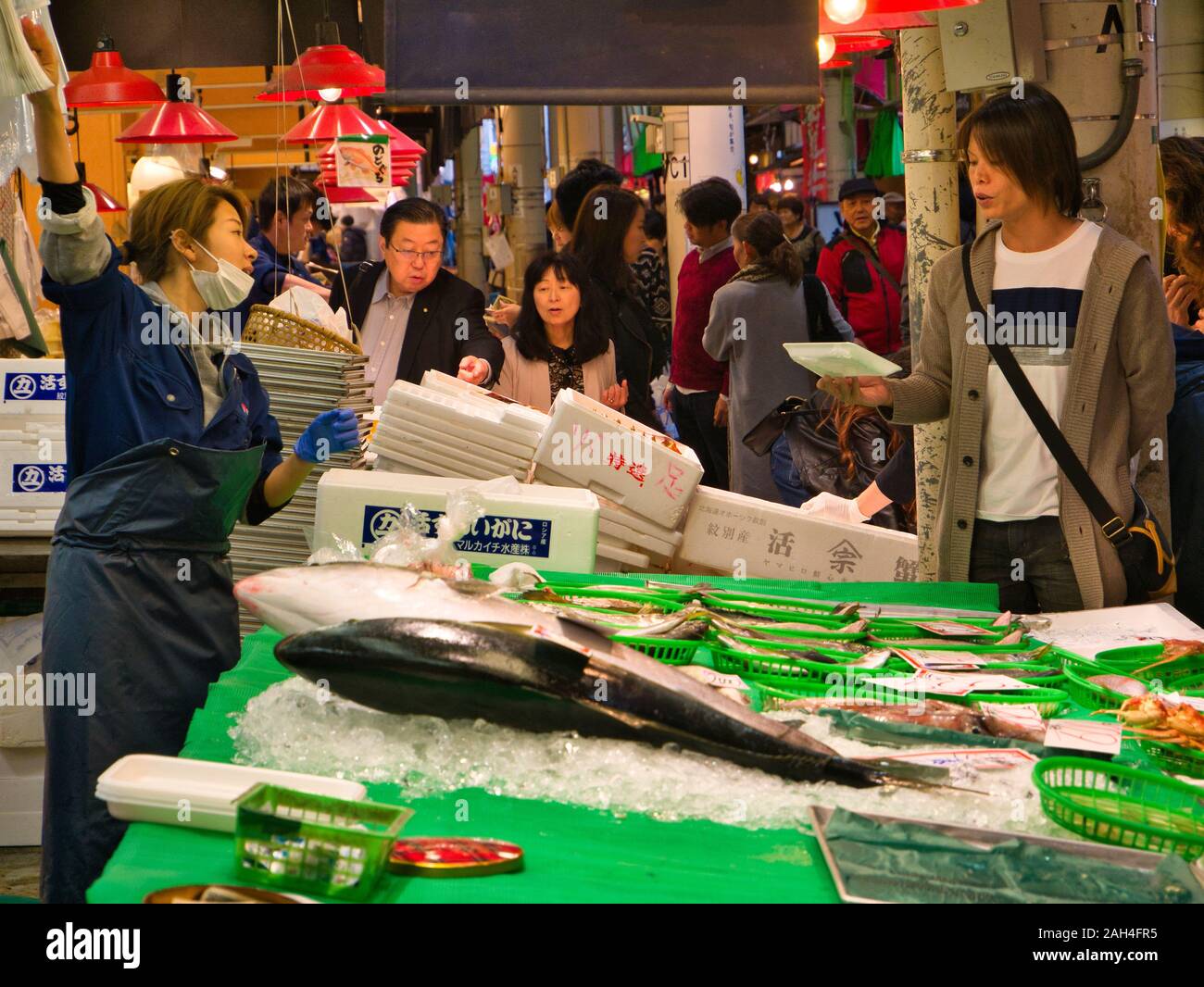 Donna che mantiene un pacchetto parla di un titolare di stallo nella trafficata Kanazawa Mercato del Pesce, Giappone. Foto Stock