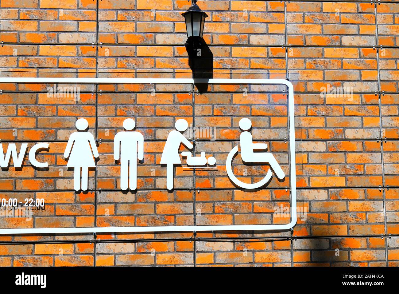In orange muro di mattoni è un wc con orientamento immagini bianche di WC, un uomo e una donna, un baby changing scena di un bambino e di una persona in sedia a rotelle. Foto Stock