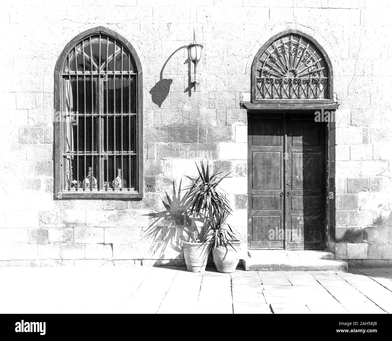In bianco e nero ad alto contrasto colpo di vecchi abbandonati mattoni di pietra della parete arcuata con porta in legno e vetro con coperta in ferro battuto e lanterna in una giornata di sole, il Cairo, Egitto Foto Stock