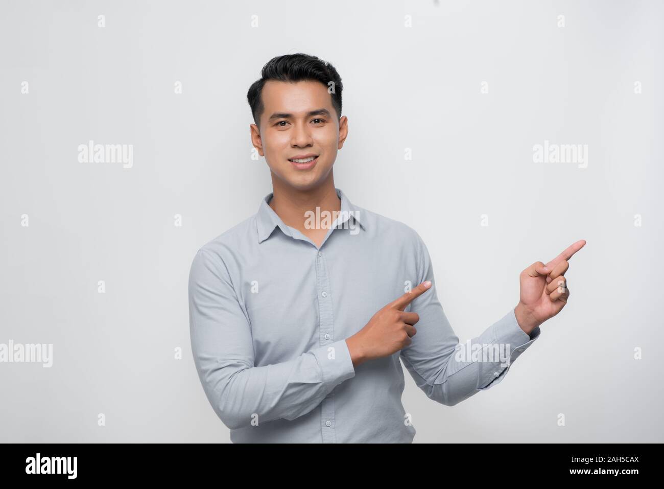 Giovane uomo asiatico sorridente e guardando la fotocamera con le due mani e le dita per lato Foto Stock