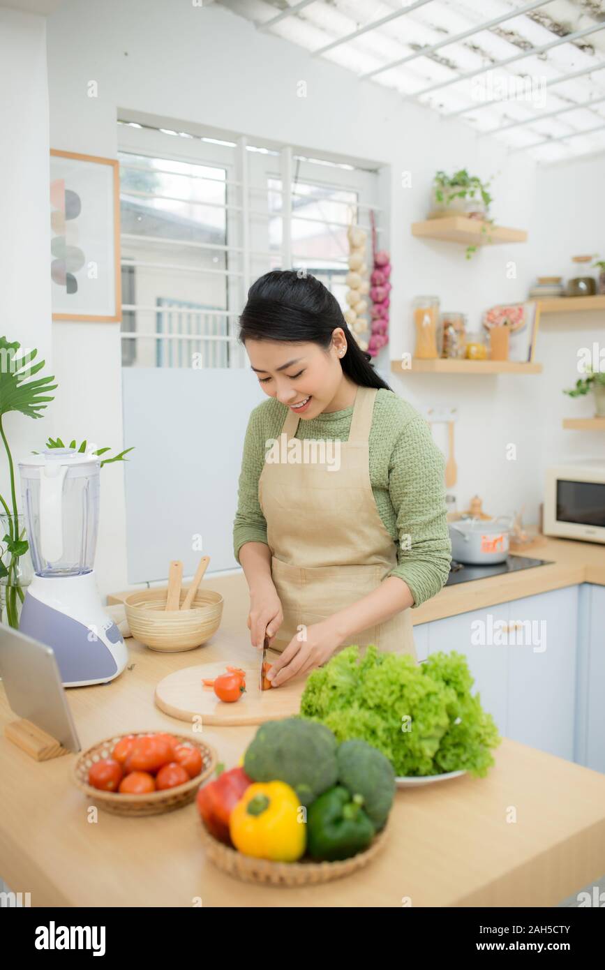 Cibo sano, dieta concetto. Donna asiatica cucina insalata di verdure per la cena, tagliare i pomodori maturi sul tagliere di legno nella cucina di casa. Foto Stock