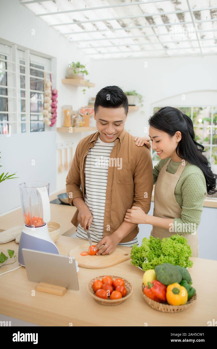 Ritratto di una bella coppia giovane cucinare insieme secondo una ricetta su un computer tablet Foto Stock