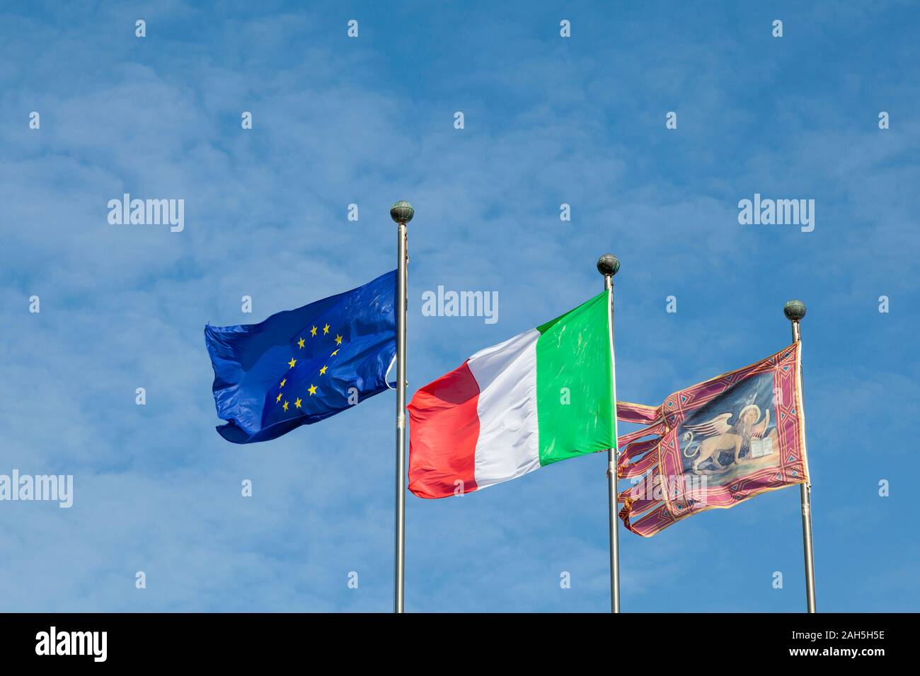 Tre bandiere con il leone di Venezia, l'Italia e la Ue o Unione europea battenti affiancati da pennoni contro un cielo blu con spazio di copia Foto Stock