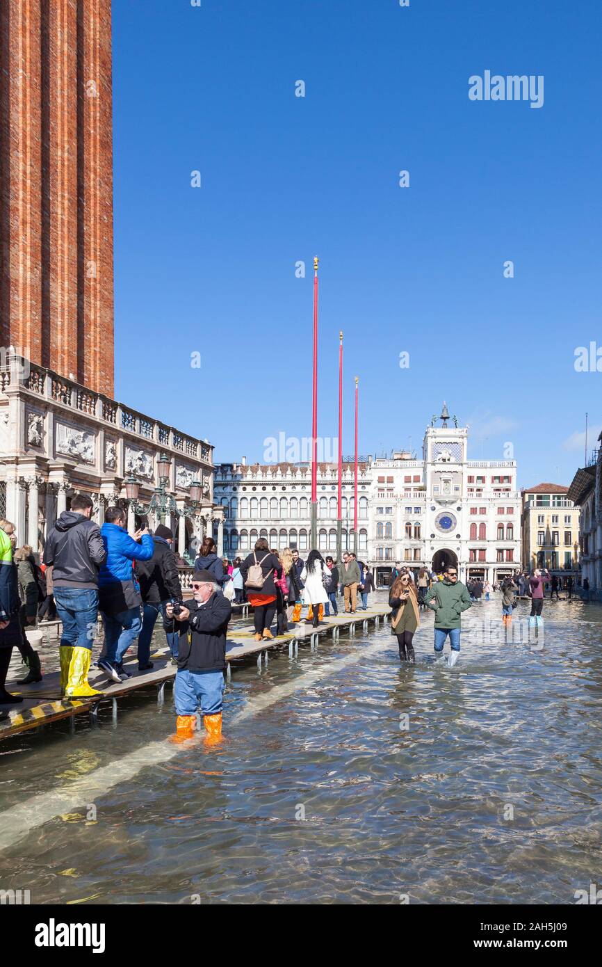Acqua Alta inondazioni durante l estrema alta marea Piazza San Marco, Venezia, Italia con i turisti a piedi su passeroles o passerelle elevate nella parte anteriore del Foto Stock