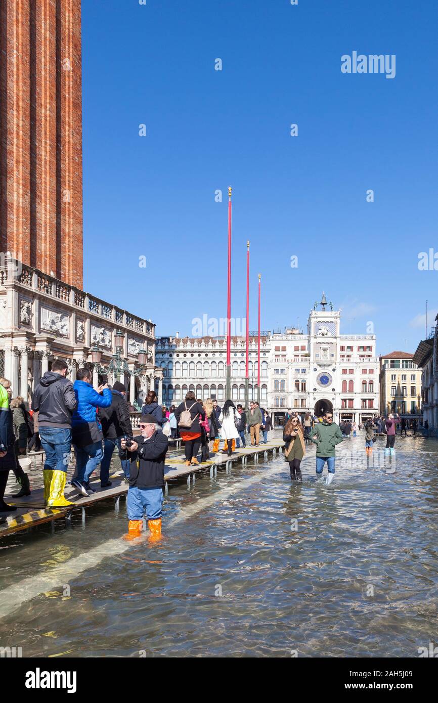 Acqua Alta inondazioni durante l estrema alta marea Piazza San Marco, Venezia, Italia con i turisti a piedi su passeroles o passerelle elevate nella parte anteriore del Foto Stock