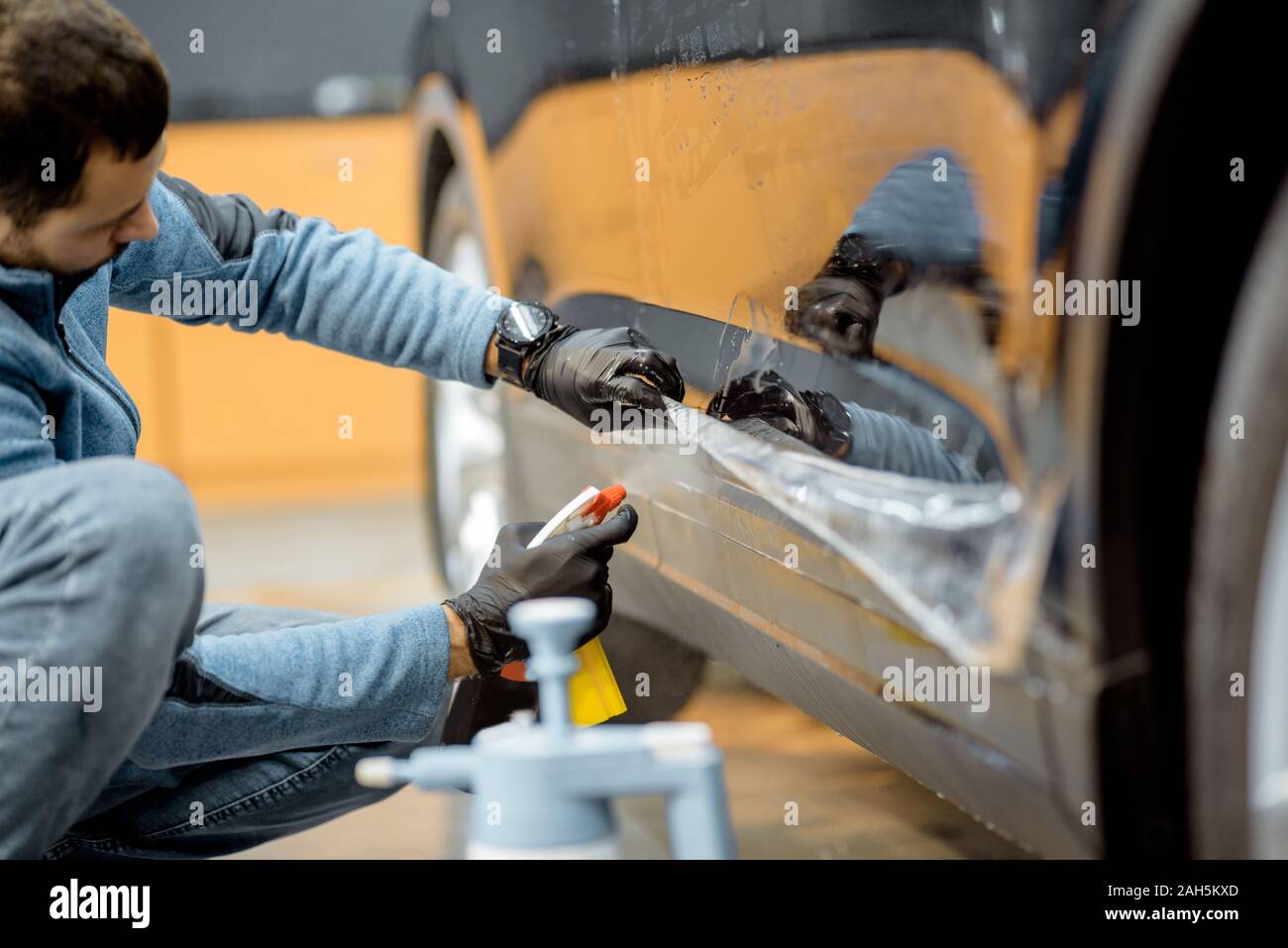 Auto di servizio lavoratore gli spruzzi di acqua sul corpo vettura, bagnando prima di anti-ghiaia film applicare al veicolo che dettaglia service Foto Stock