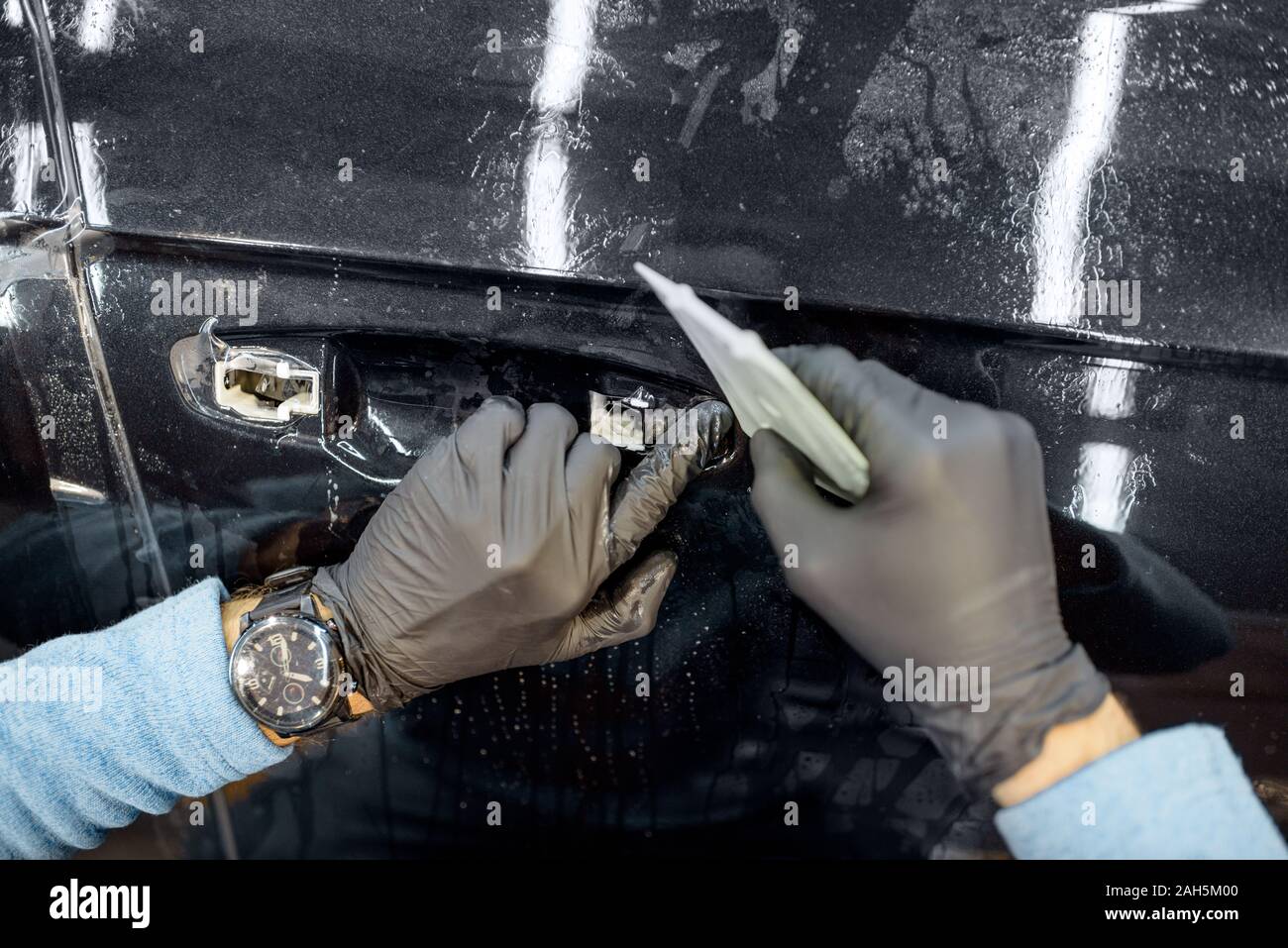 Grippaggio del lavoratore di protezione pellicola trasparente su un corpo vettura al posto della maniglia della porta, vista da vicino Foto Stock