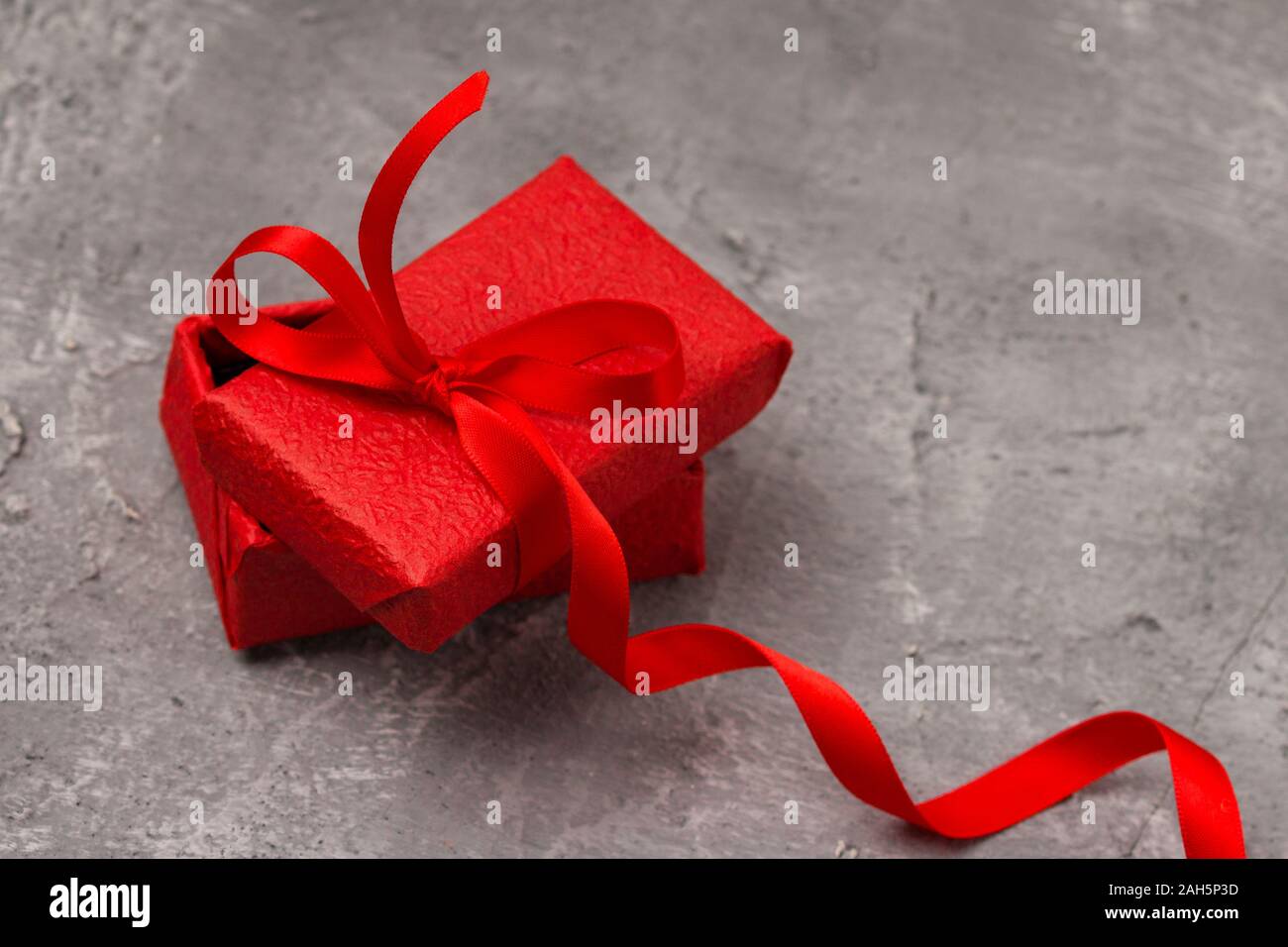 Confezione regalo rossa sul cemento grigio sfondo, copia dello spazio. Natale, capodanno, festa di compleanno, il giorno di san valentino Foto Stock
