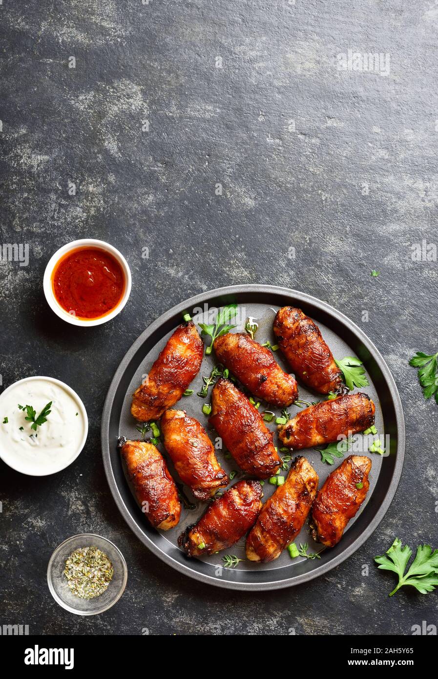 Pancetta avvolto grigliate di ali di pollo sulla piastra su pietra nera sfondo con spazio libero per il testo. Gustosi snack da carne di pollo, pancetta dolce, aspro Foto Stock