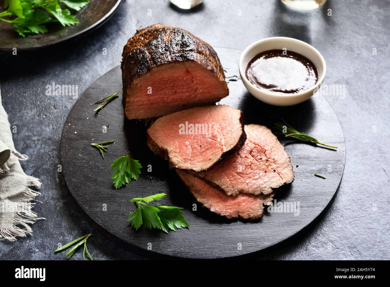 Fette di manzo alla griglia sulla tavola di legno su pietra scura sullo sfondo. Foto Stock