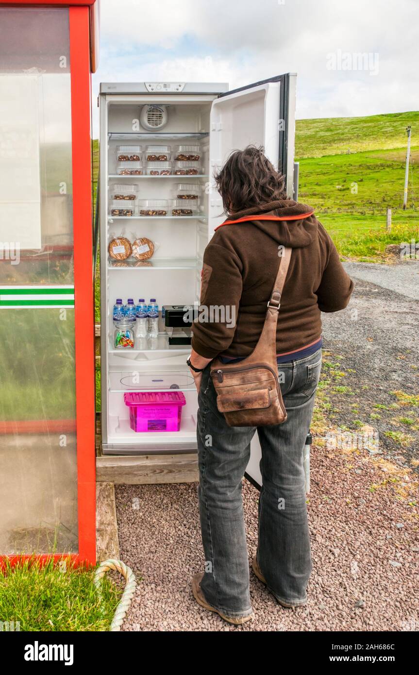 Una fame donna analizzando il contenuto di sabbia onestà nella casella 'frigo sulla terraferma Shetland. Foto Stock