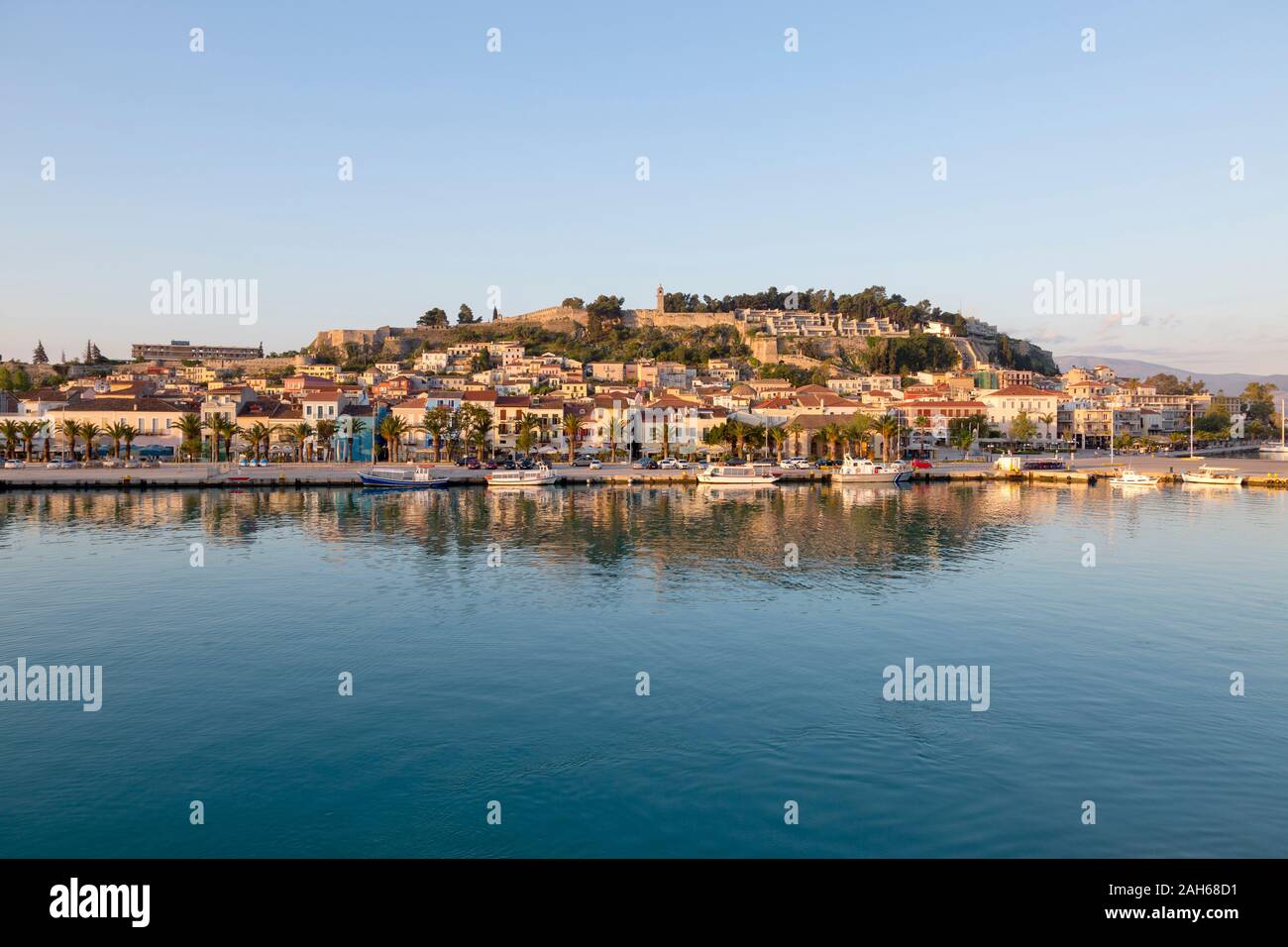 Vista di Nafplio, con i suoi riflessi nelle calme acque del porto su una soleggiata mattina di primavera, con cieli blu. La fortezza di Palamidi siede sulla parte superiore della città. Foto Stock