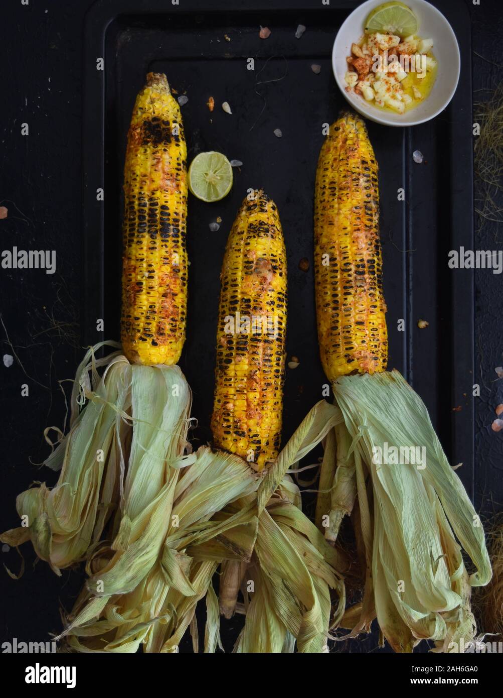 Mais alla griglia su cob con formaggio, paprika, sale marino e calce, indian street food, mais arrostito su una piastra nera, idee per barbecue e grill party Foto Stock