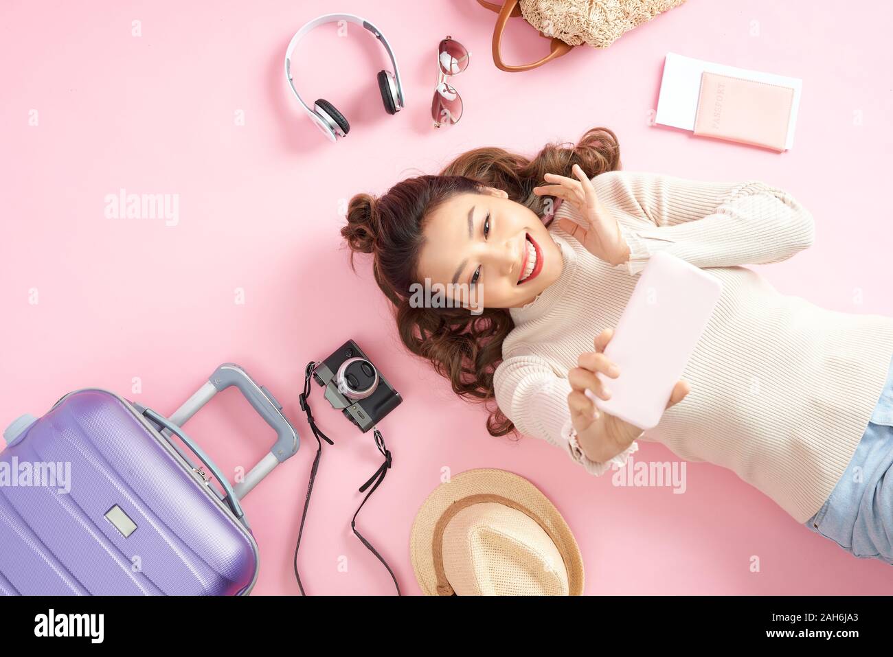 Bella giovane donna selfie sul pavimento di colore rosa con il suo bagaglio di viaggio. Vista superiore Foto Stock