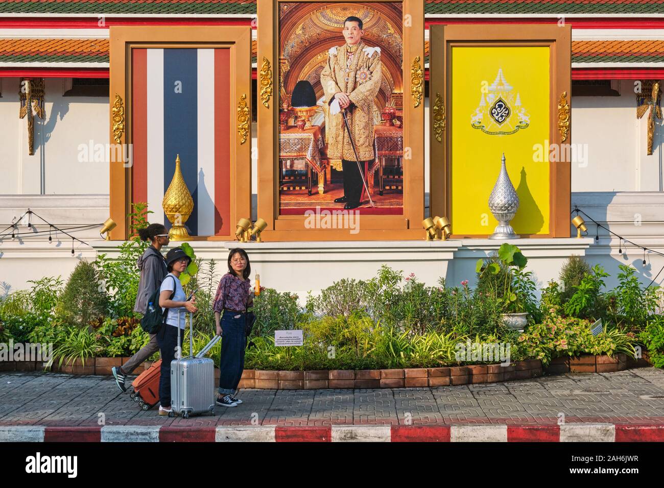 I turisti con valigie passare sotto un ritratto di Re Tailandese Maha Vajiralongkorn lungo la parete est di Wat Po (Pho), Bangkok, Thailandia Foto Stock