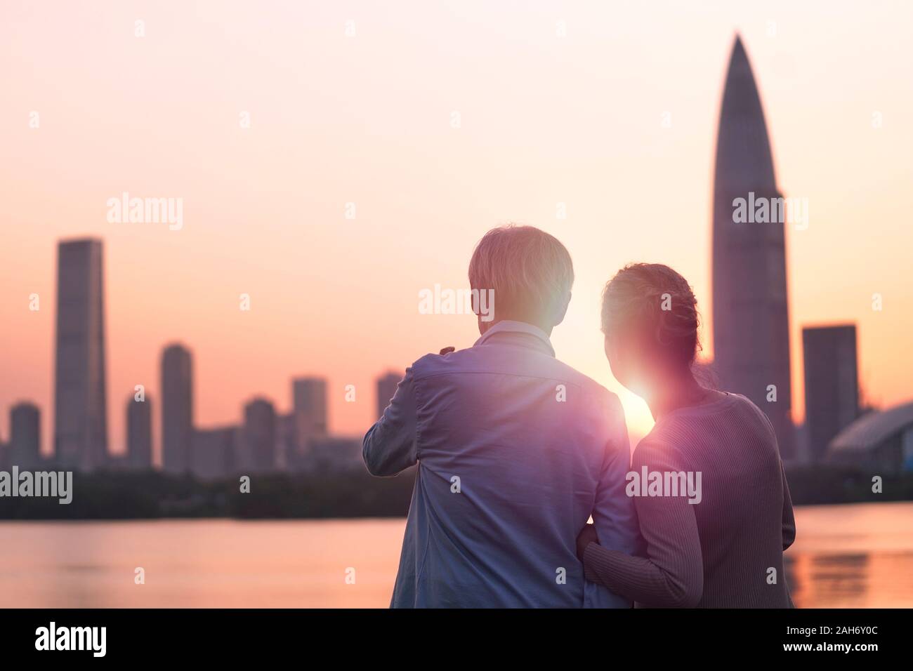 Vista posteriore del senior asian coppia in cerca di sunrise e dello skyline della città di Fiume Foto Stock