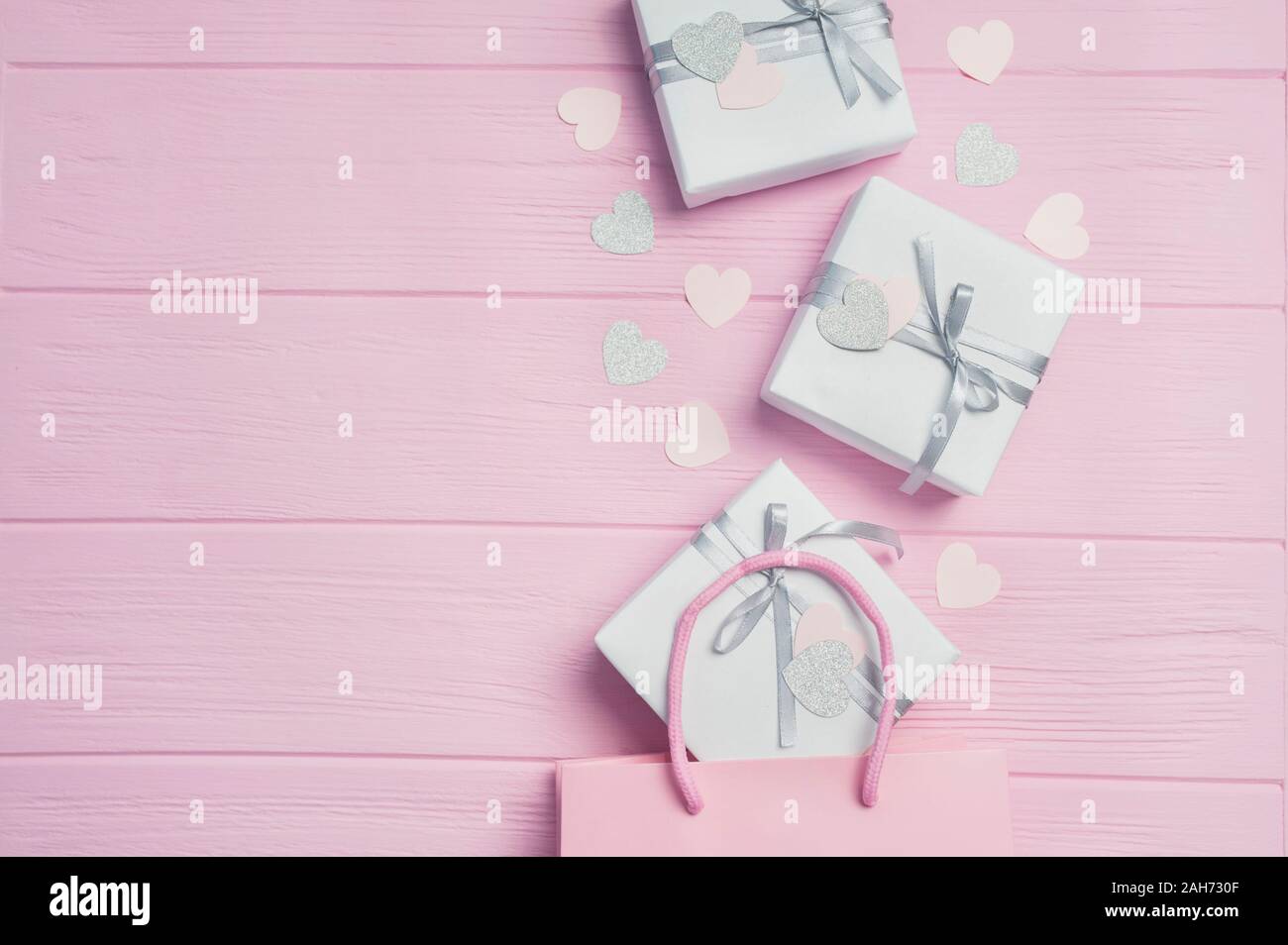 Dono scatole bianche d'argento con nastro di raso dal pacchetto rosa e coriandoli a forma di cuore su sfondo rosa. Mock up su Womens Day, il giorno di San Valentino Foto Stock