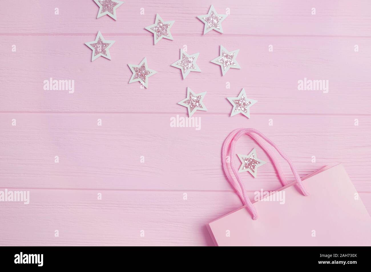 Natale Anno Nuovo Lay piatto mock up e auguri di compleanno vista superiore rosa borsa regalo e glitter coriandoli a forma di stelle su legno di rosa Foto Stock