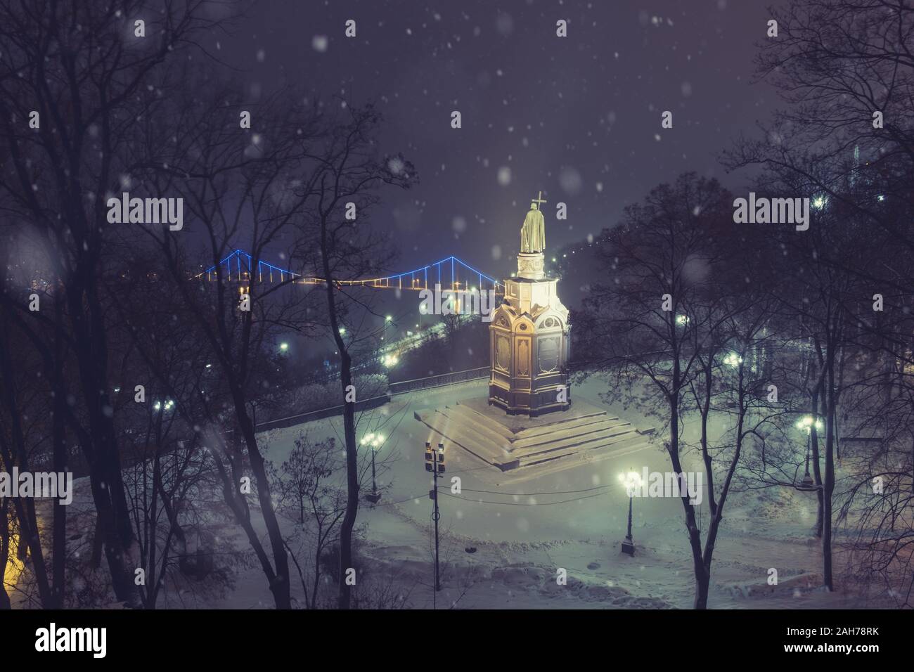 Illuminata la statua in bronzo di San Vladimiro in inverno di Kiev. Smerigliato fiume Dnieper e ponte pedonale a sfondo. L'Ucraina Foto Stock