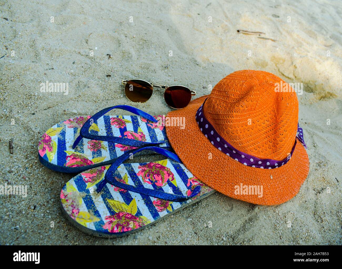 Orange hat, flip-flop e occhiali da sole sulla bianca spiaggia di sabbia Foto Stock