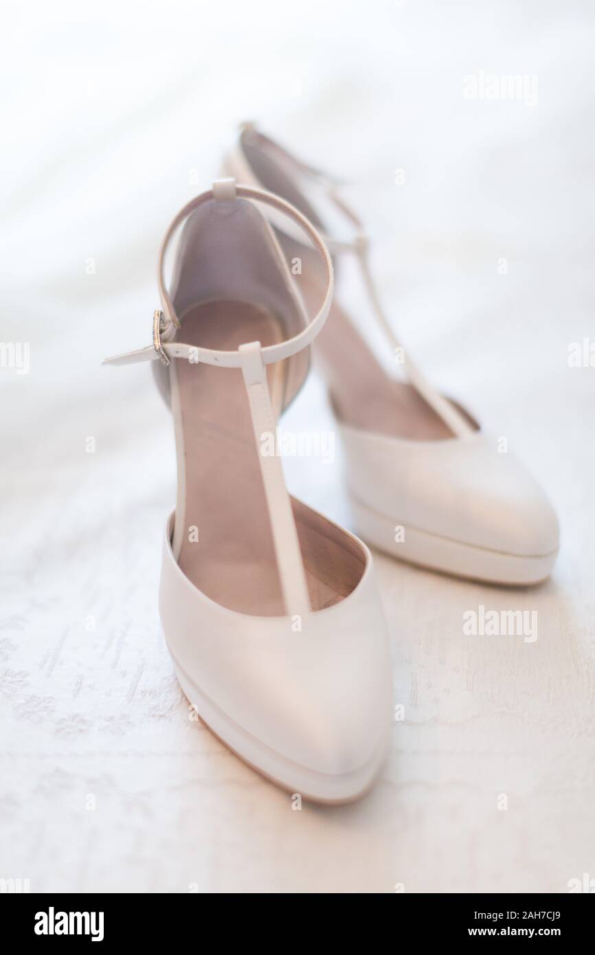 Primo piano di un paio di scarpe da sposa bianche con tacchi alti, giacenti su una copertura bianca del letto Foto Stock