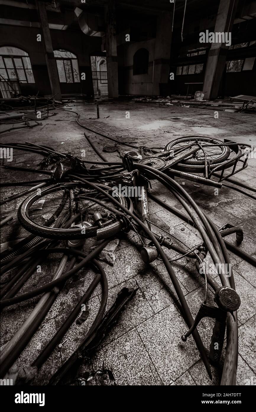 Ampio angolo di visione in bianco e nero di un pavimento abbandonato della fabbrica, con una bicicletta scartata in primo piano Foto Stock