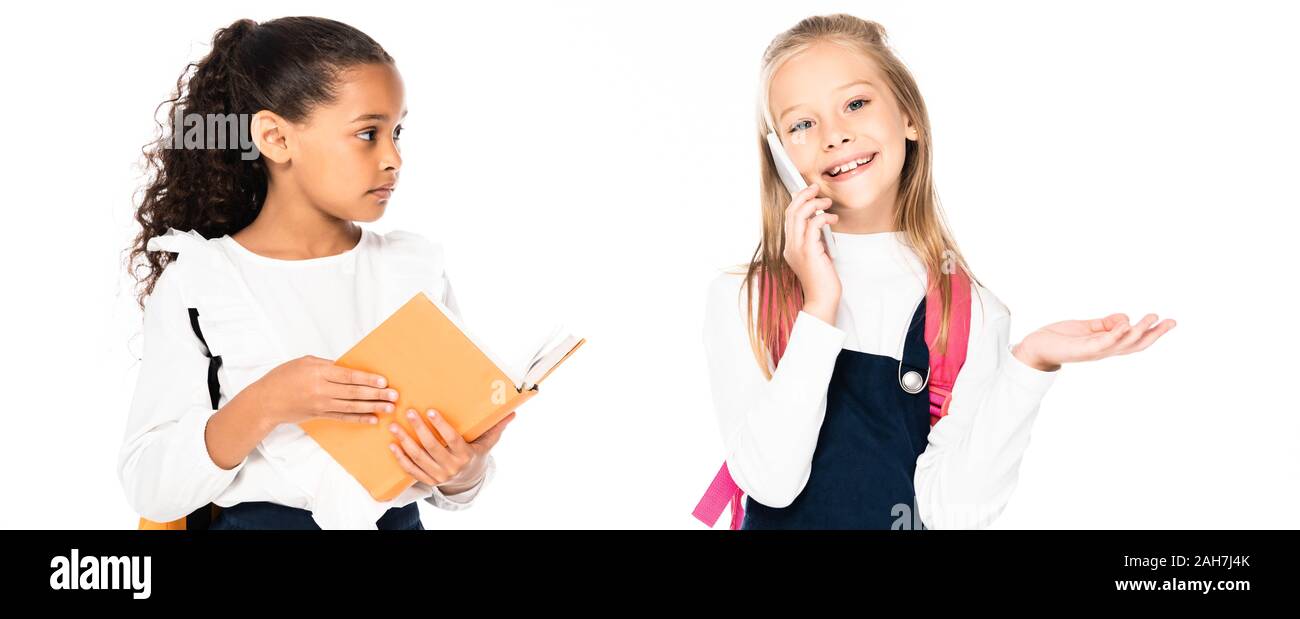 Panoramica di orinato african american schoolgirl guardando allegro amico parlando sullo smartphone isolato su bianco Foto Stock