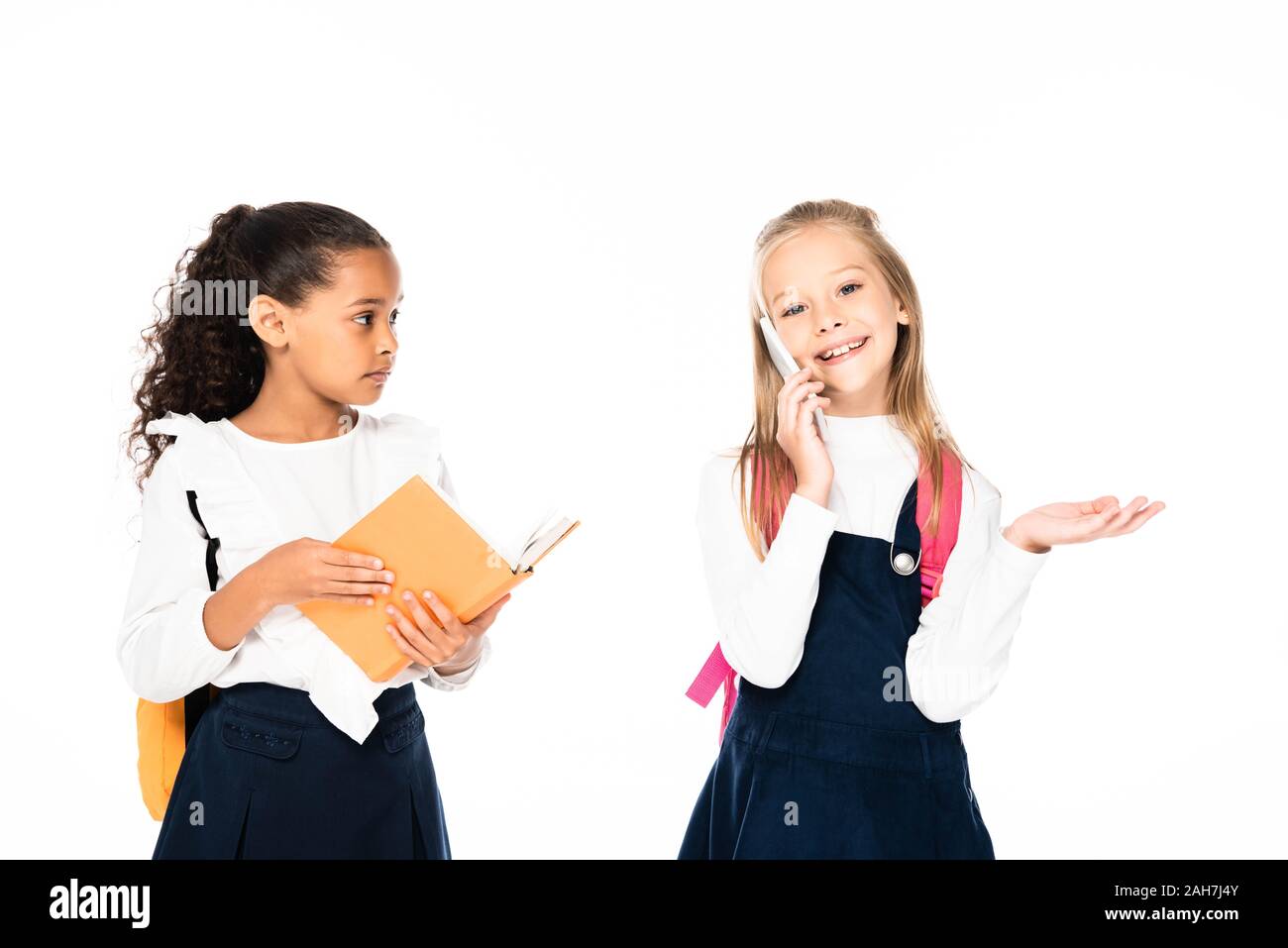 Orinato African American schoolgirl azienda prenota e guardando amico parlando sullo smartphone isolato su bianco Foto Stock