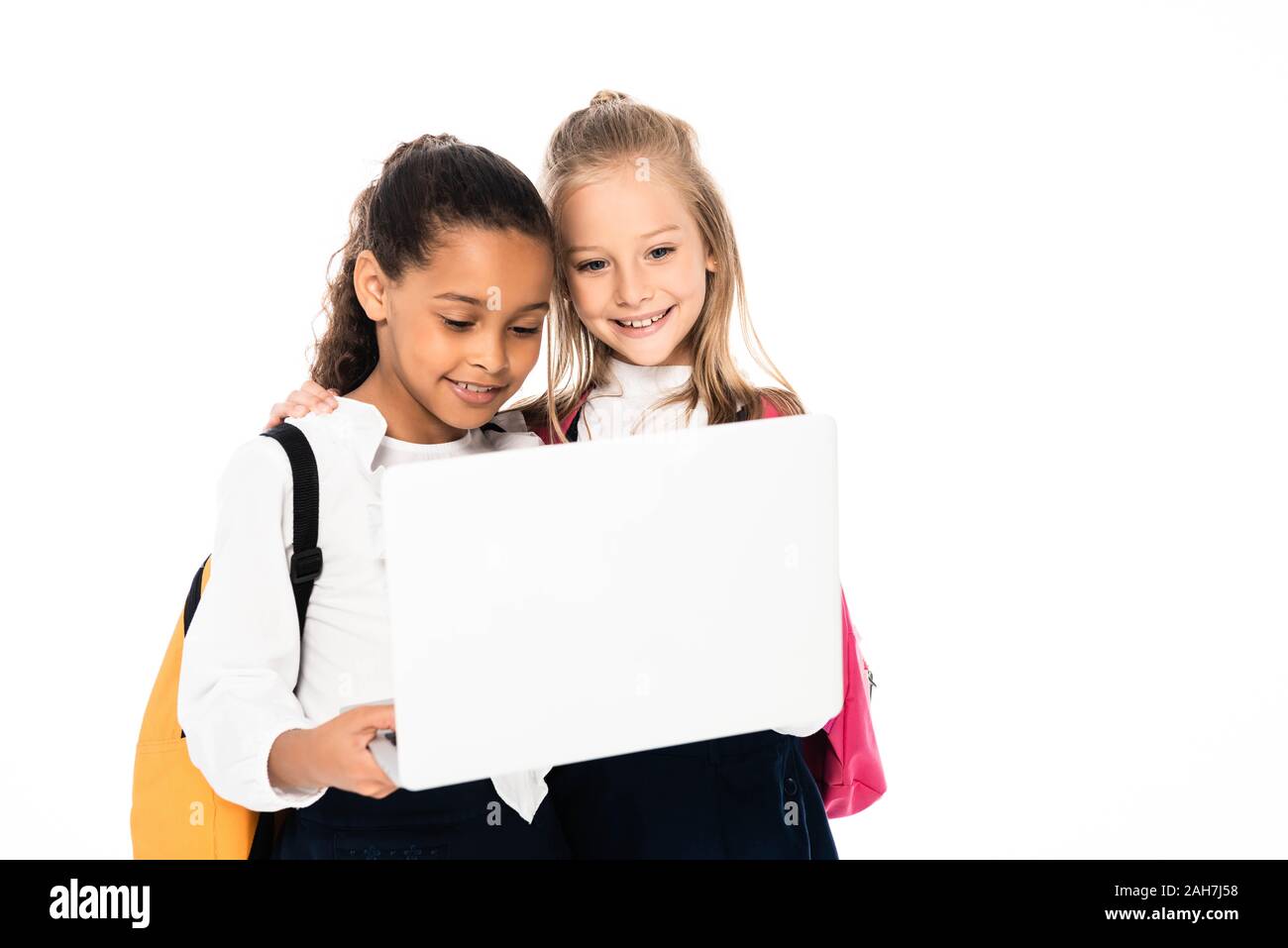 Due allegro multiculturale di studentesse sorridere mentre utilizzando computer portatile isolato su bianco Foto Stock
