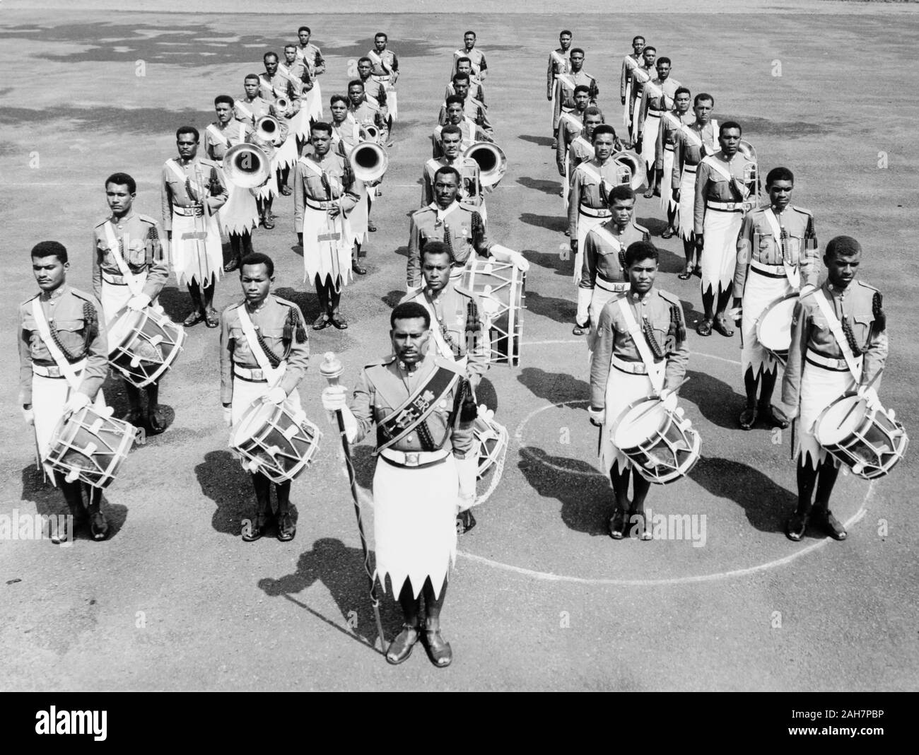 Isole Figi, Royal Fijiano BandFronted militari da un grande tamburo tenendo un personale, 32-pezzo Royal Fijiano banda militare sta nella formazione, pronto a marzo. La band di strumenti includono tamburi, tromboni, tube e trombe. La didascalia recita: questa famosa banda del Fijiano forze militari ha girato in molti paesi in tutto il mondo, 1965. 2005/010/1/14/9. Foto Stock