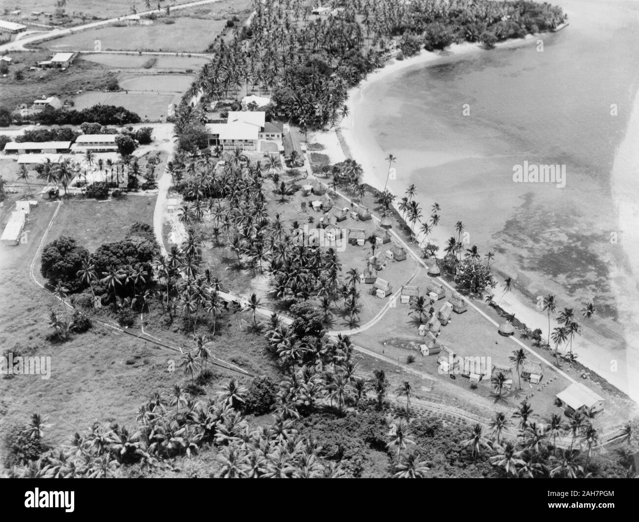 Le isole Figi, l'Koralevu Beach Hotel, FijiAerial vista del Koralevu Beach Hotel, situato a metà strada tra le città di Nadi e Suva. Un certo numero di Fijian di stile "Bure' (abitazioni), utilizzato per accogliere turisti, sedersi in gruppi lungo il lungomare. La didascalia recita: vista aerea del famoso Koralevu beach hotel - a metà strada tra Nadi e Suva. Nota il nativo di molti "Bure' per i visitatori, 1965. 2005/010/1/14/78. Foto Stock