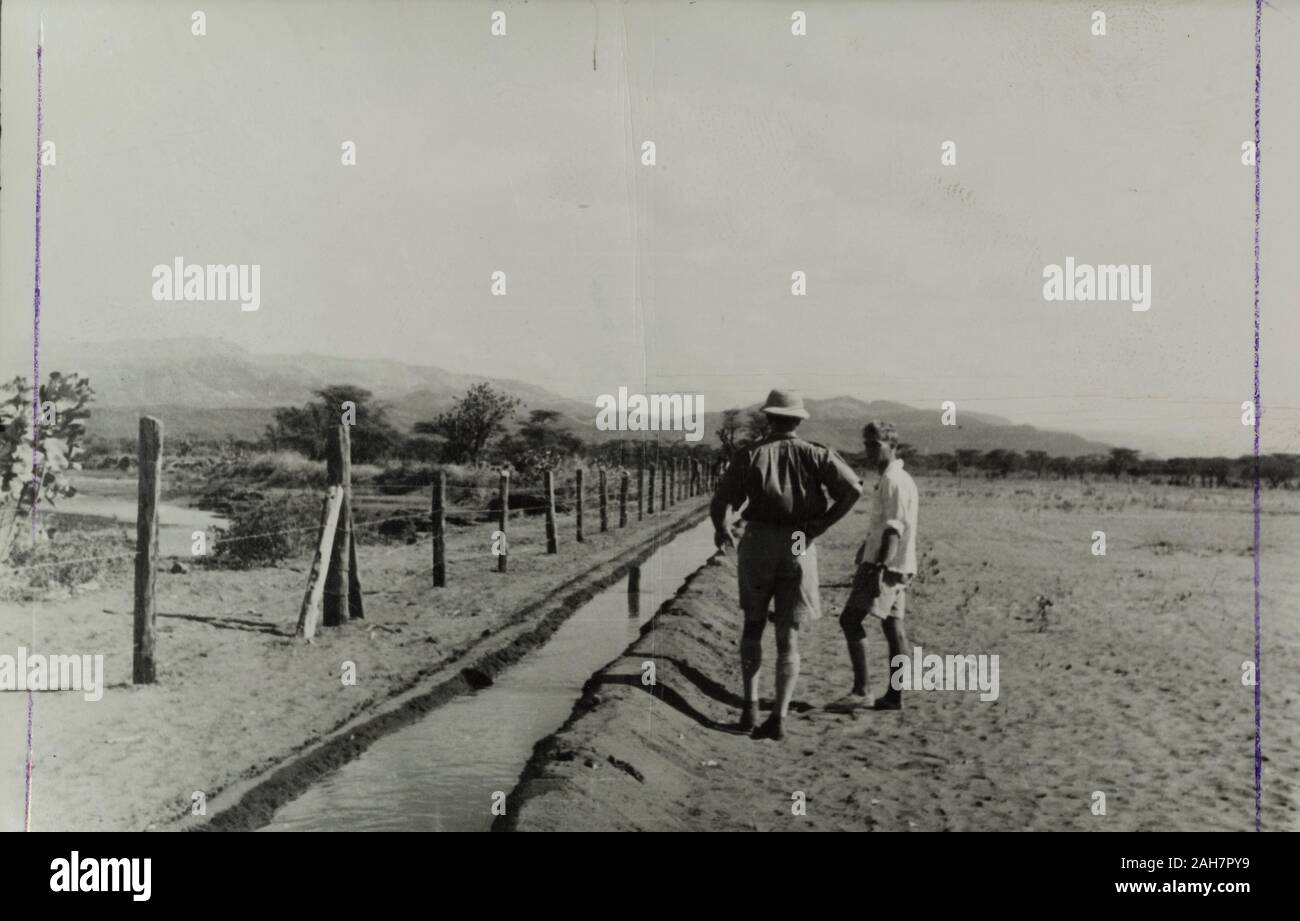 Kenya, due europei ispezionare un canale di irrigazione, costruito da Mau Mau detenuti come parte di un programma di riabilitazione. Manoscritto originale didascalia: Perherra schema di riabilitazione. La scherma pianura sottostante Embu, 1953. 1995/076/1/1/15/8.16. Foto Stock