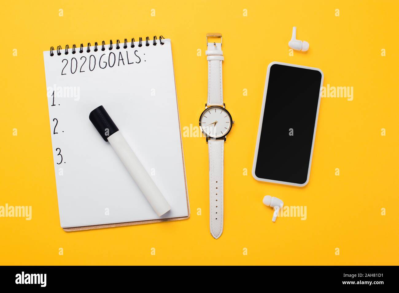 Notebook con obiettivi 2020 Iscrizione e vuoto di punti numerati nei pressi di smartphone, orologio da polso e auricolari wireless sulla superficie gialla Foto Stock