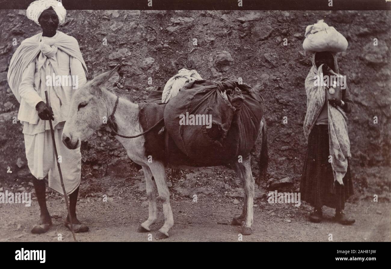 India, una 'dhobi' (laundryman), raffigurata con un asino carico di sacchi di biancheria. Una donna si erge accanto all'asino con un sacchetto equilibrato sul suo capo.manoscritto originale didascalia: Dhoby, circa 1900. 2003/071/1/1/3/42. Foto Stock